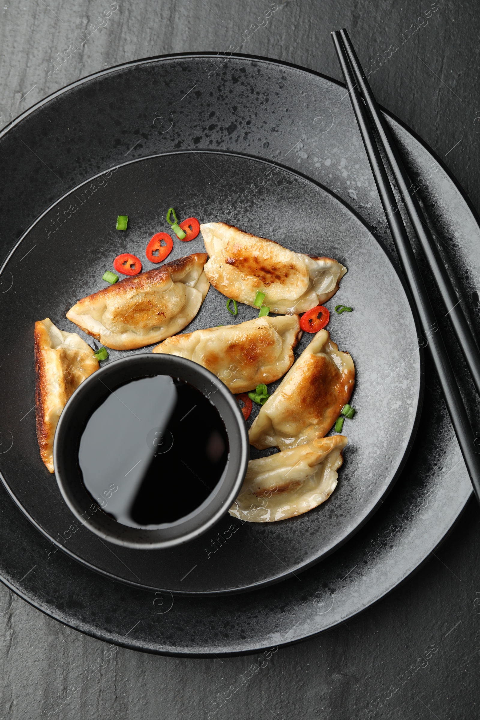 Photo of Delicious fried gyoza dumplings with green onions and chili peppers served on black table, top view