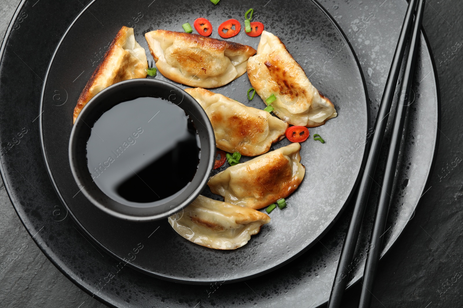 Photo of Delicious fried gyoza dumplings with green onions and chili peppers served on black table, top view