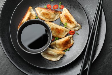 Photo of Delicious fried gyoza dumplings with green onions and chili peppers served on black table, top view