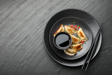 Photo of Delicious fried gyoza dumplings with green onions and chili peppers served on black table, top view. Space for text