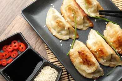 Photo of Delicious fried gyoza dumplings with sesame seeds served on wooden table, closeup