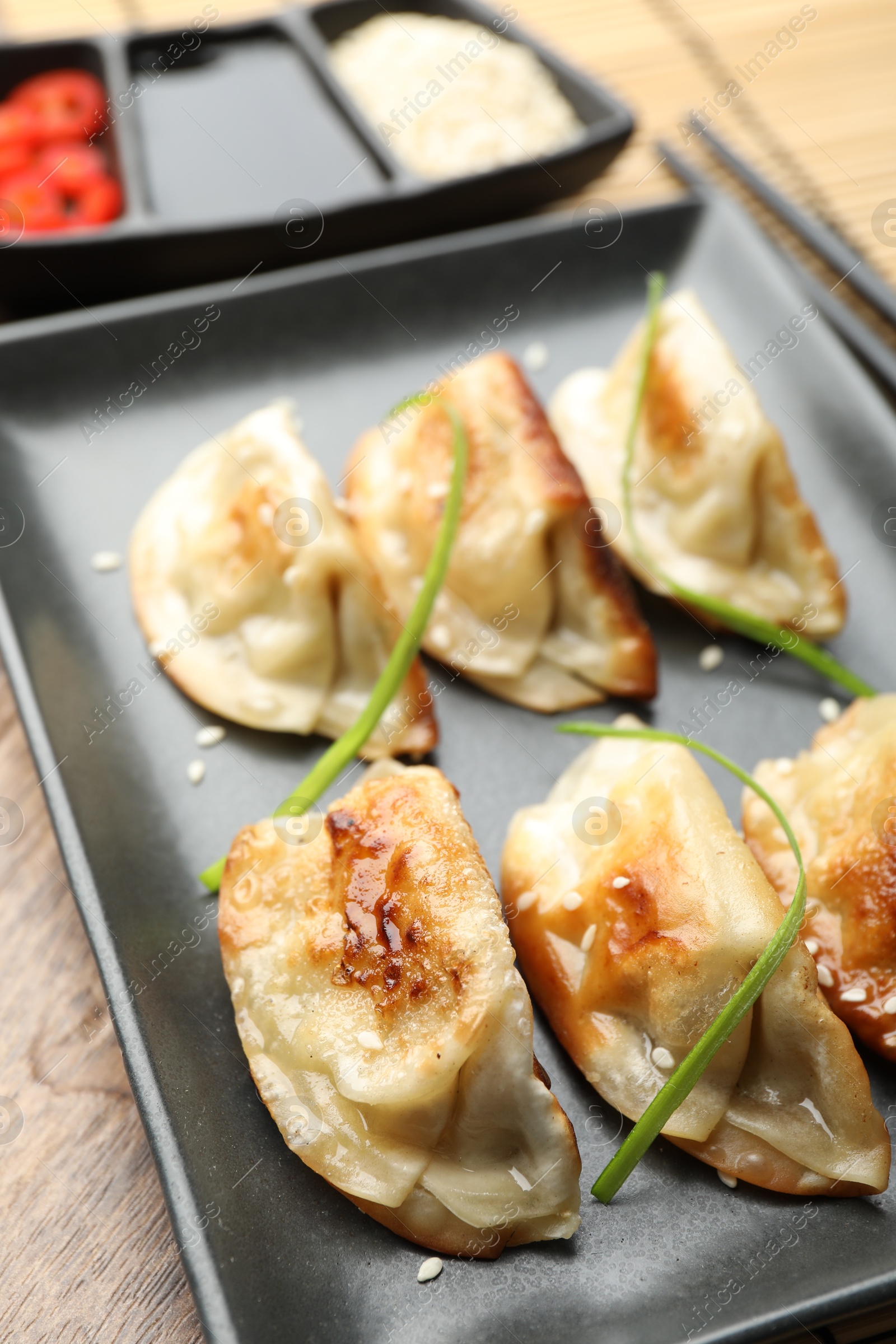 Photo of Delicious fried gyoza dumplings with sesame seeds served on wooden table, closeup