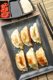 Photo of Delicious fried gyoza dumplings with sesame seeds served on wooden table, flat lay