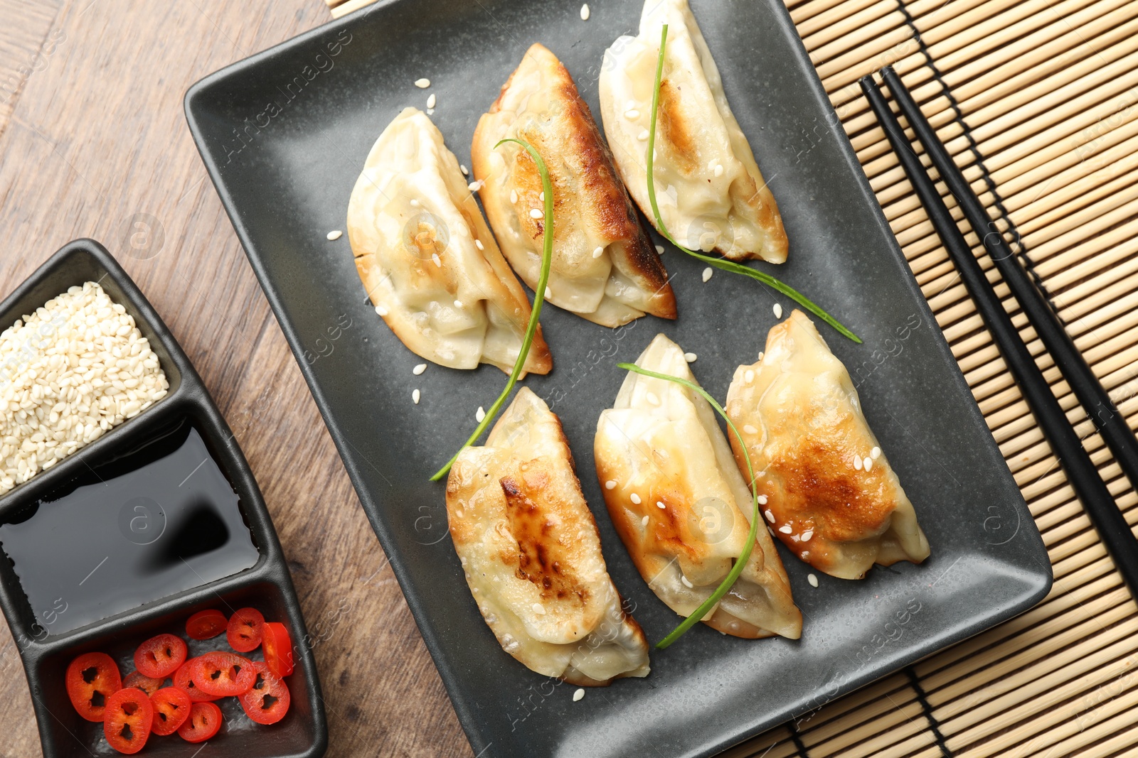 Photo of Delicious fried gyoza dumplings with sesame seeds served on wooden table, flat lay