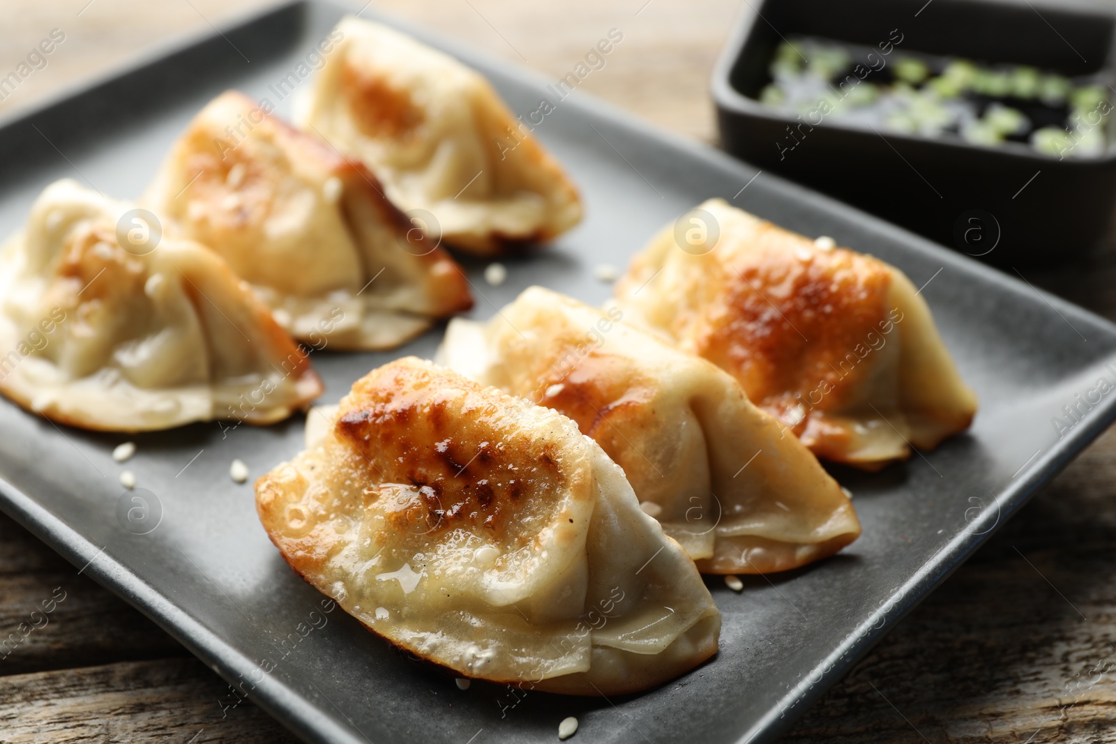 Photo of Fried gyoza dumplings with sesame seeds on wooden table, closeup