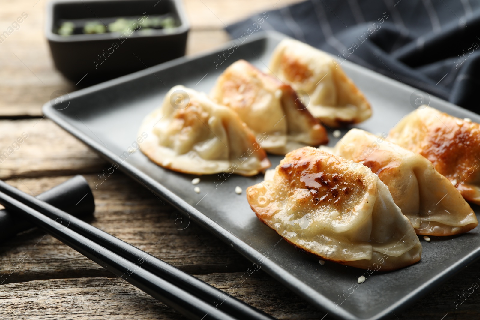 Photo of Delicious fried gyoza dumplings with sesame seeds served on wooden table, closeup