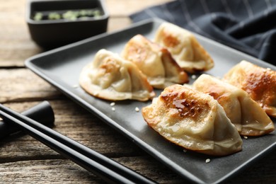 Photo of Delicious fried gyoza dumplings with sesame seeds served on wooden table, closeup