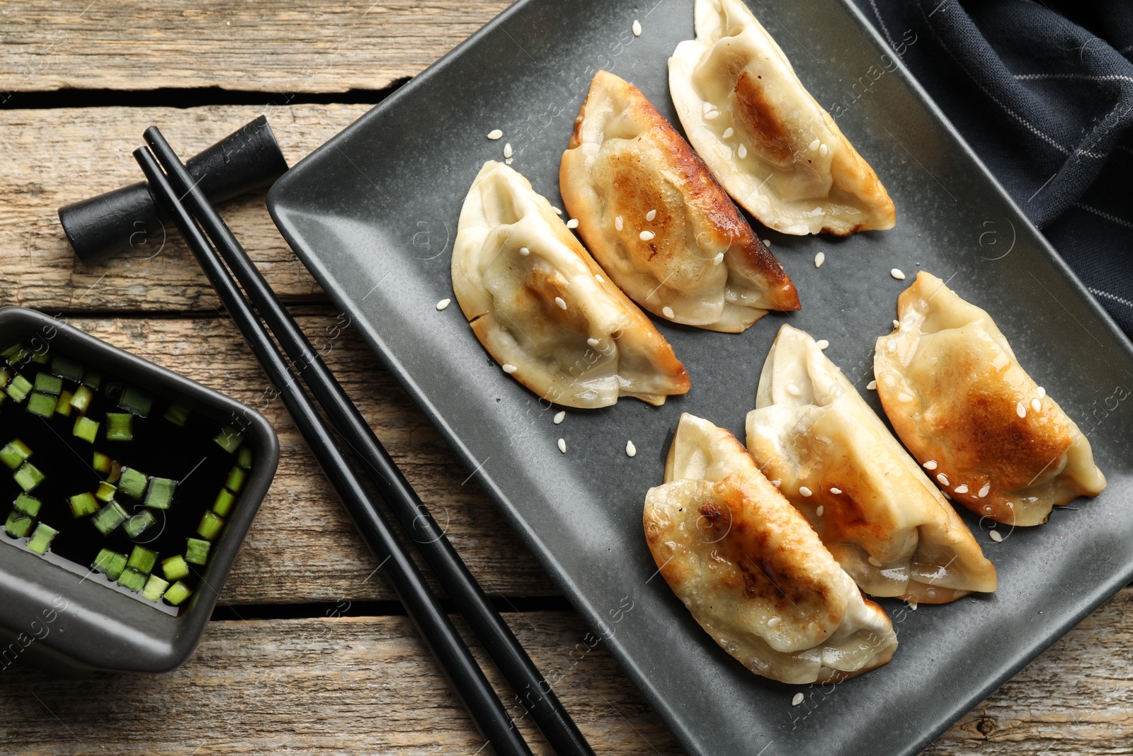 Photo of Delicious fried gyoza dumplings with sesame seeds served on wooden table, flat lay