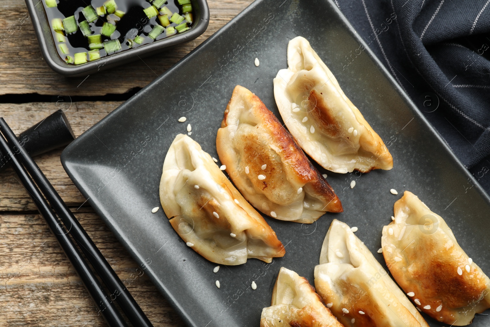 Photo of Delicious fried gyoza dumplings with sesame seeds served on wooden table, flat lay