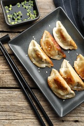 Photo of Delicious fried gyoza dumplings with sesame seeds served on wooden table, flat lay