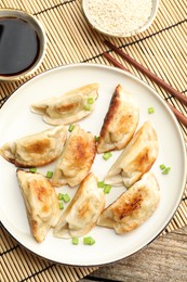 Photo of Delicious fried gyoza dumplings with green onions served on wooden table, flat lay