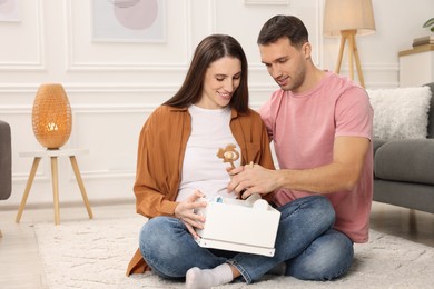 Photo of Pregnant woman and her husband with box of baby toys at home