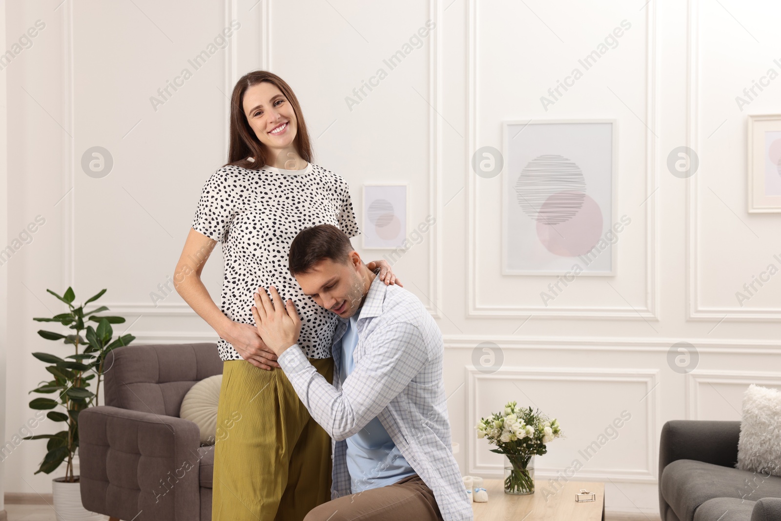 Photo of Man listening to baby in his pregnant wife's belly at home. Space for text