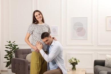 Photo of Man listening to baby in his pregnant wife's belly at home. Space for text