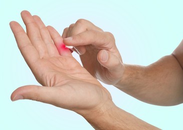 Image of Man with joint inflammation applying cream on light blue background, closeup