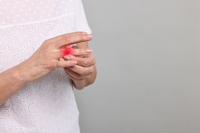 Woman with joint inflammation on grey background, closeup. Red area on finger