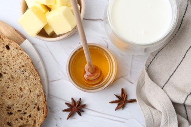 Photo of Sweet honey, butter, bread and milk on white table, flat lay