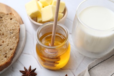 Photo of Sweet honey, butter, bread and milk on white table, closeup