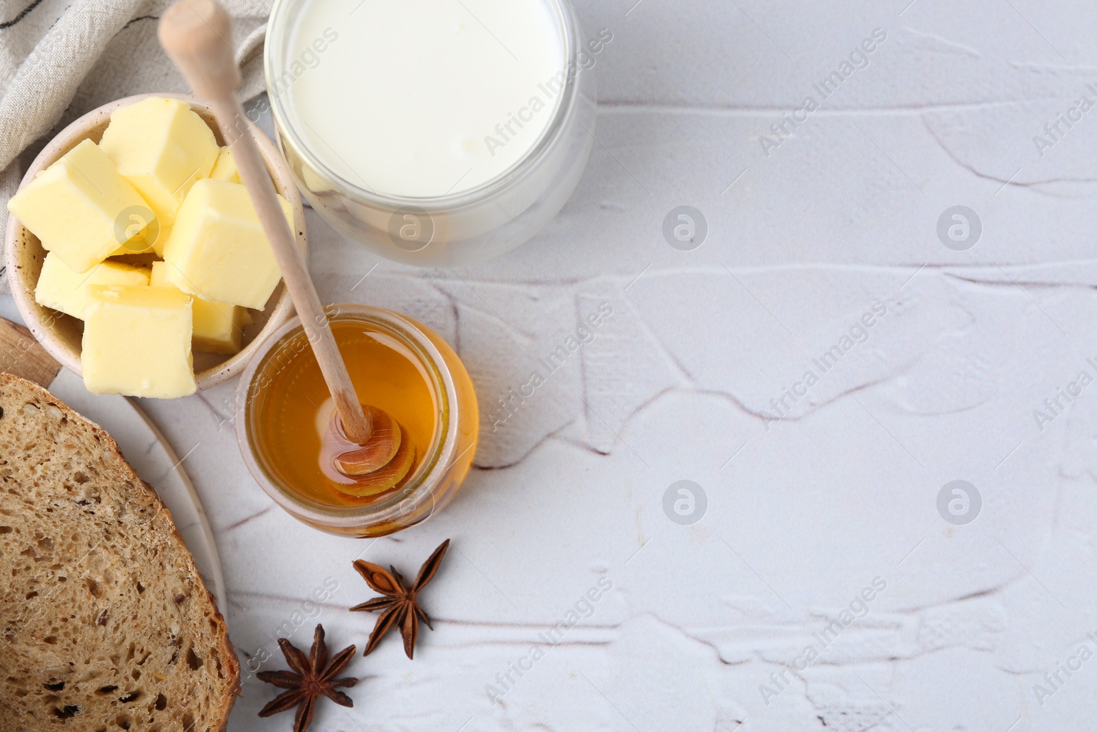 Photo of Sweet honey, butter, bread and milk on white table, flat lay. Space for text