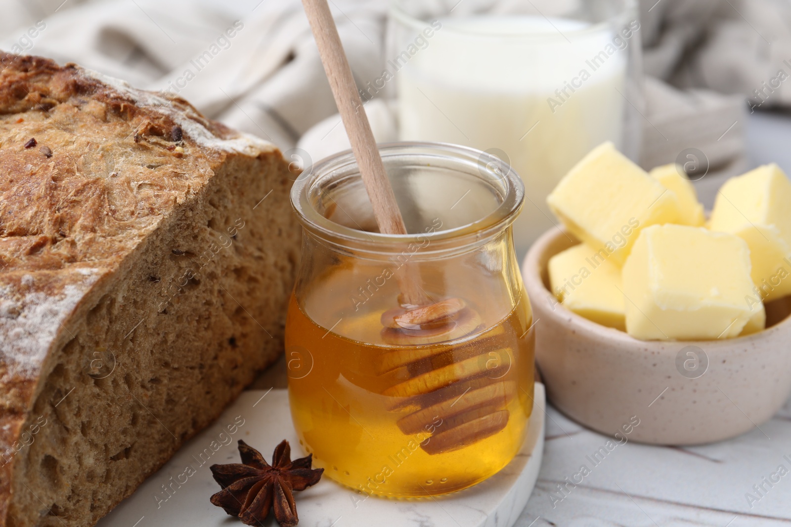 Photo of Sweet honey, butter, bread and milk on white table, closeup