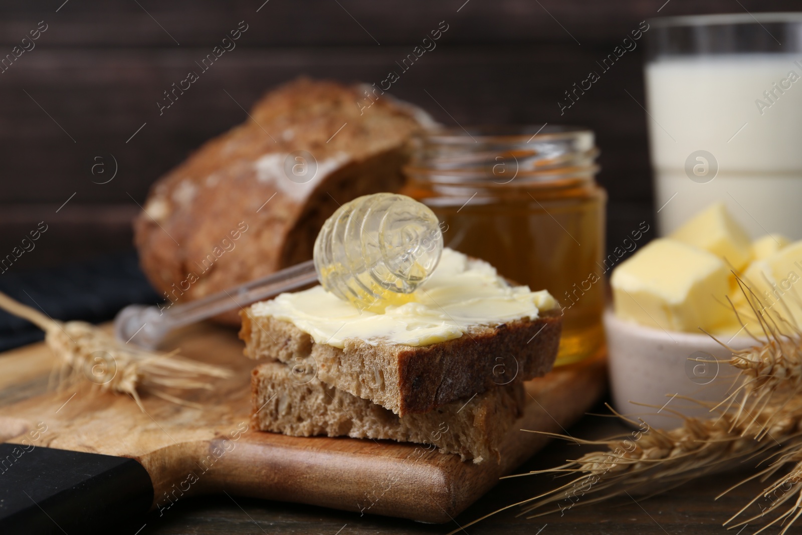 Photo of Tasty sandwich with butter, honey, dipper and milk on wooden table, closeup