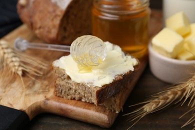 Photo of Tasty sandwich with butter, honey and dipper on wooden table, closeup