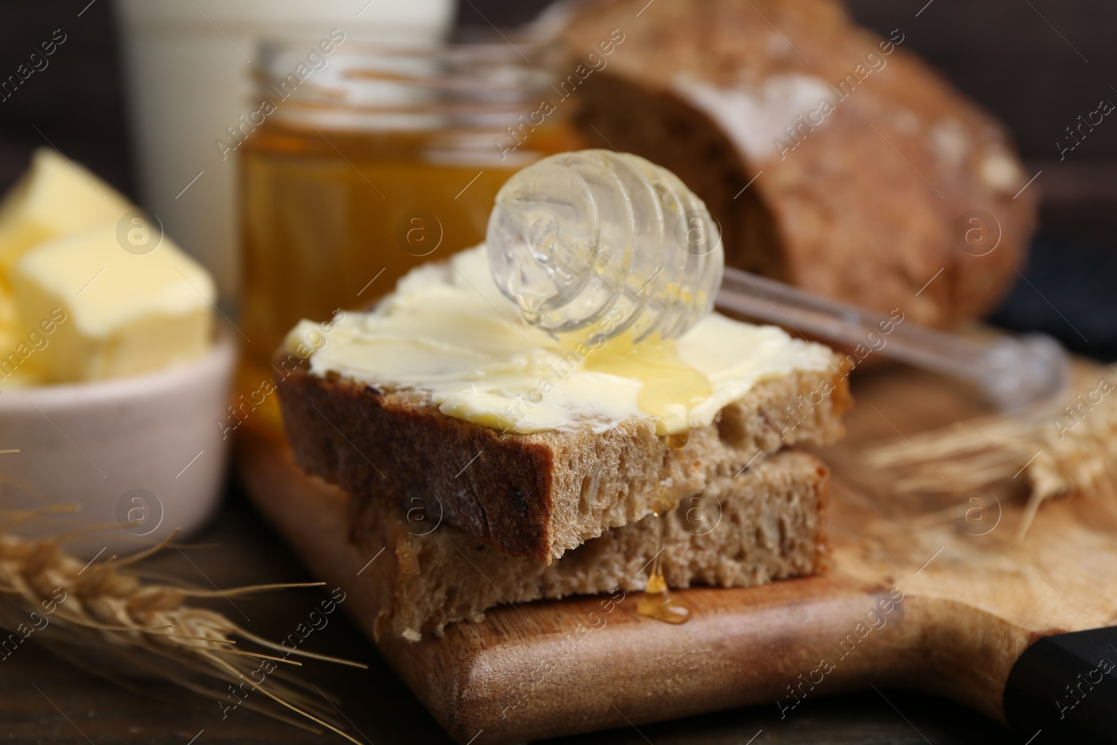 Photo of Tasty sandwich with butter, honey and dipper on wooden table, closeup