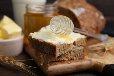 Photo of Tasty sandwich with butter, honey and dipper on wooden table, closeup