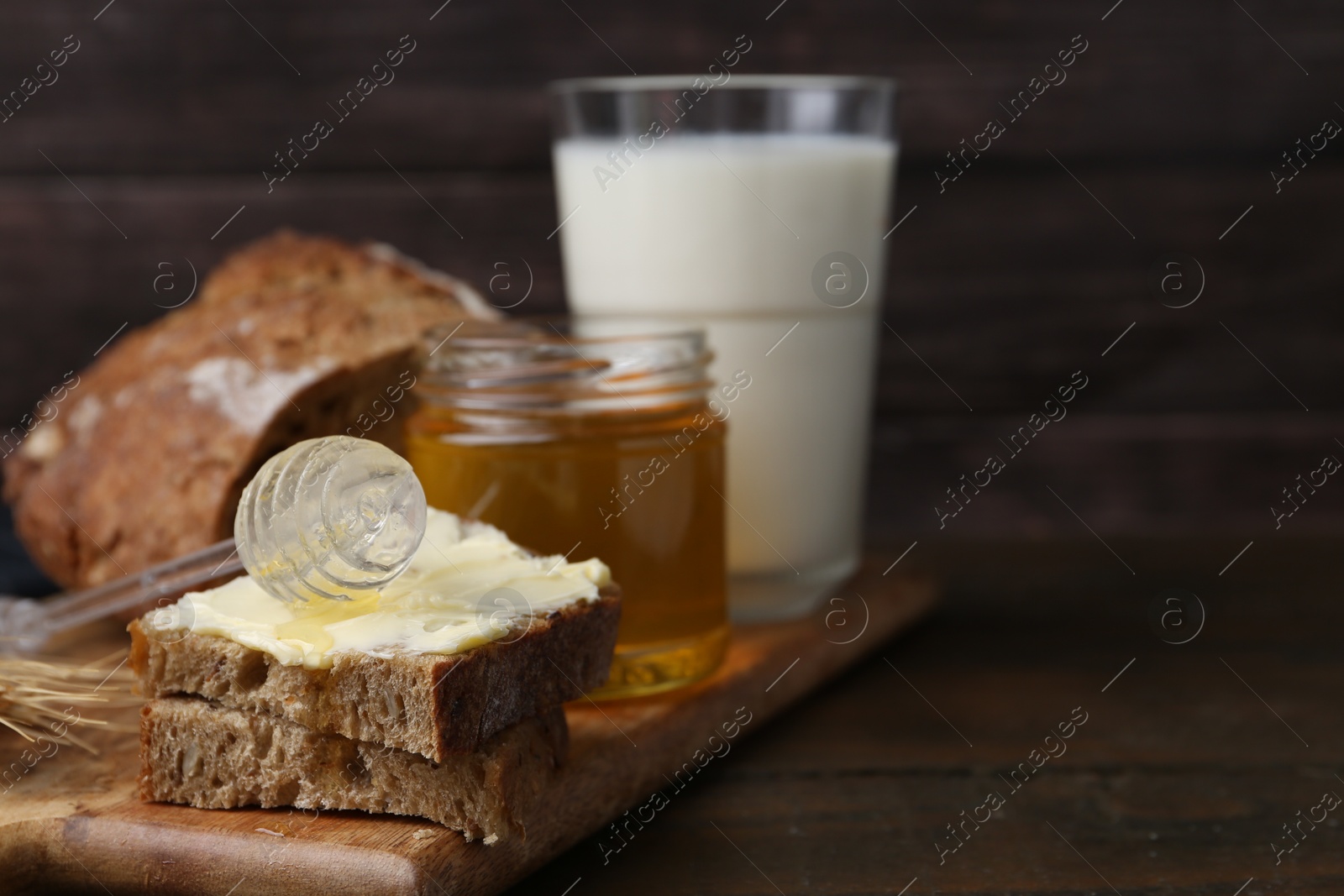 Photo of Tasty sandwich with butter, honey, dipper and milk on wooden table, closeup. Space for text