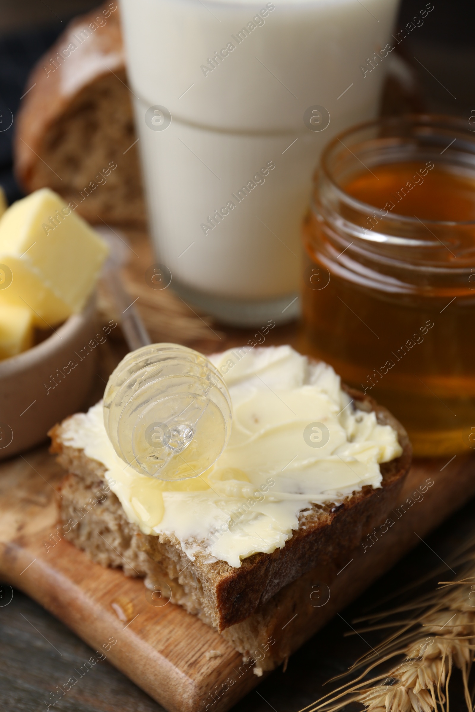 Photo of Tasty sandwich with butter, honey, dipper and milk on wooden table, closeup