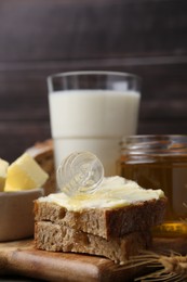 Photo of Tasty sandwich with butter, honey and dipper on wooden table, closeup