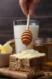 Woman pouring honey onto sandwich at wooden table, closeup