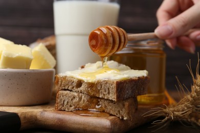 Photo of Woman pouring honey onto sandwich at wooden table, closeup