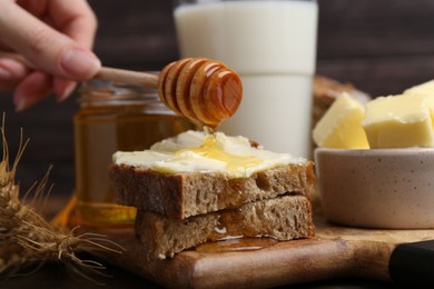 Photo of Woman pouring honey onto sandwich at wooden table, closeup