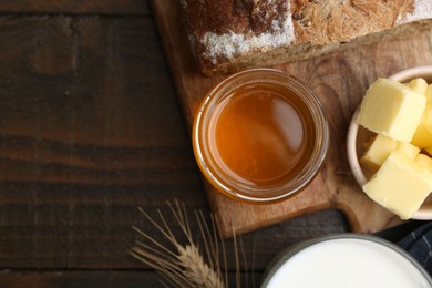 Sweet honey, butter, bread and milk on wooden table, flat lay. Space for text