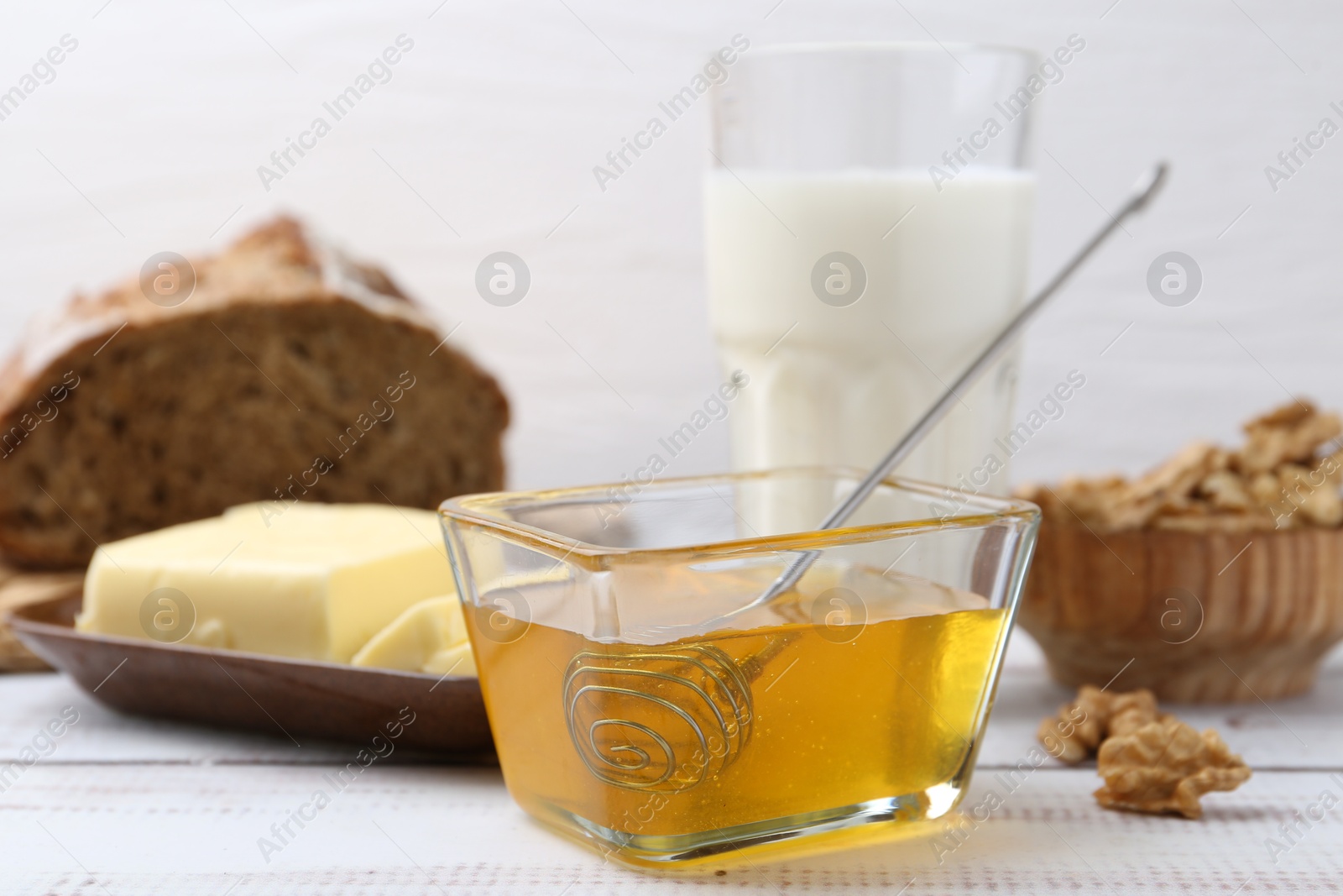 Photo of Sweet honey, butter, walnuts and milk on white wooden table, closeup