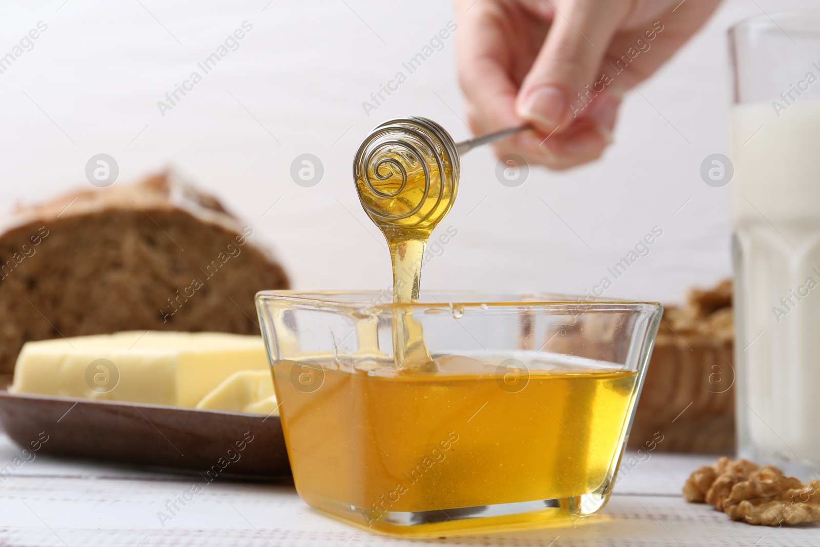 Photo of Woman taking honey with dipper at white wooden table, closeup