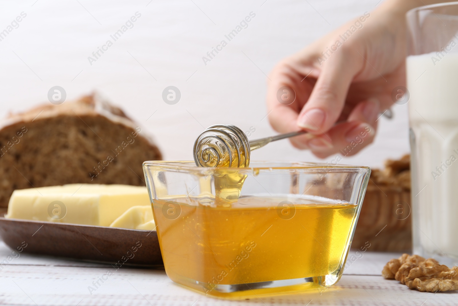 Photo of Woman taking honey with dipper at white wooden table, closeup