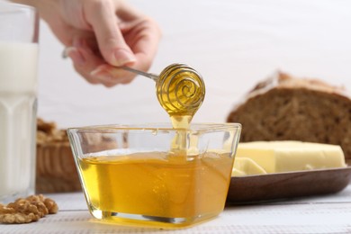 Photo of Woman taking honey with dipper at white wooden table, closeup