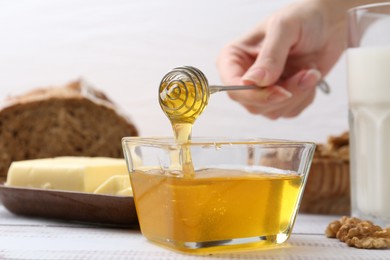 Photo of Woman taking honey with dipper at white wooden table, closeup