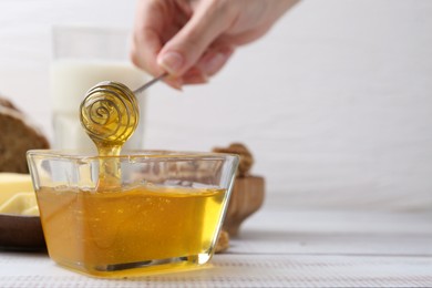 Photo of Woman taking honey with dipper at white wooden table, closeup. Space for text