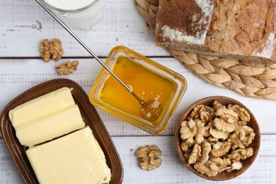 Photo of Sweet honey, butter, bread and walnuts on white wooden table, flat lay