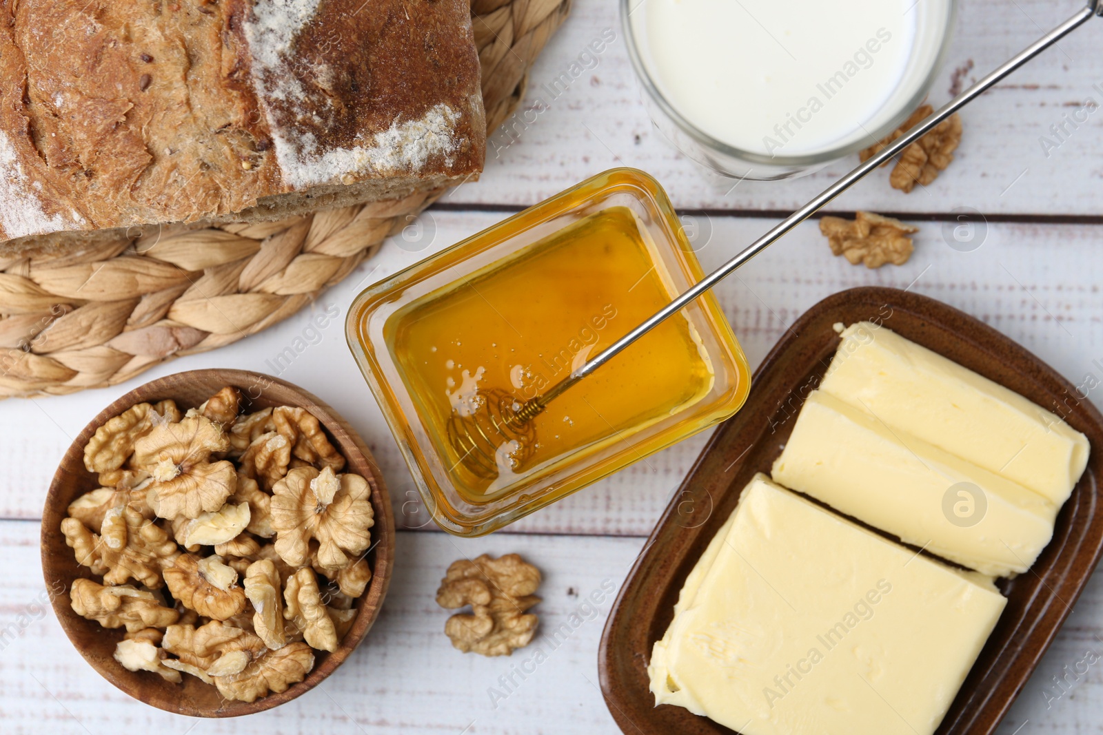 Photo of Sweet honey, butter, milk, bread and walnuts on white wooden table, flat lay