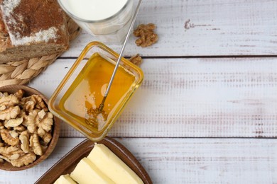 Photo of Sweet honey, butter, milk, bread and walnuts on white wooden table, flat lay. Space for text