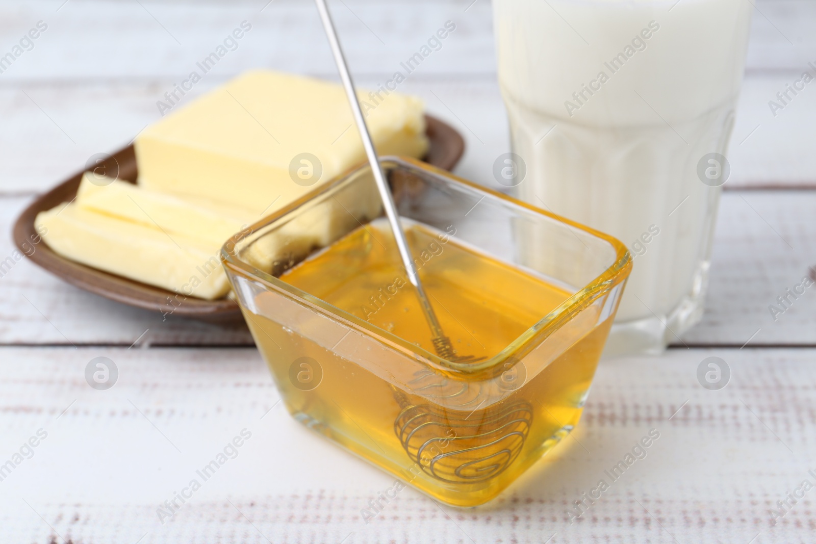 Photo of Sweet honey, butter and milk on white wooden table, closeup