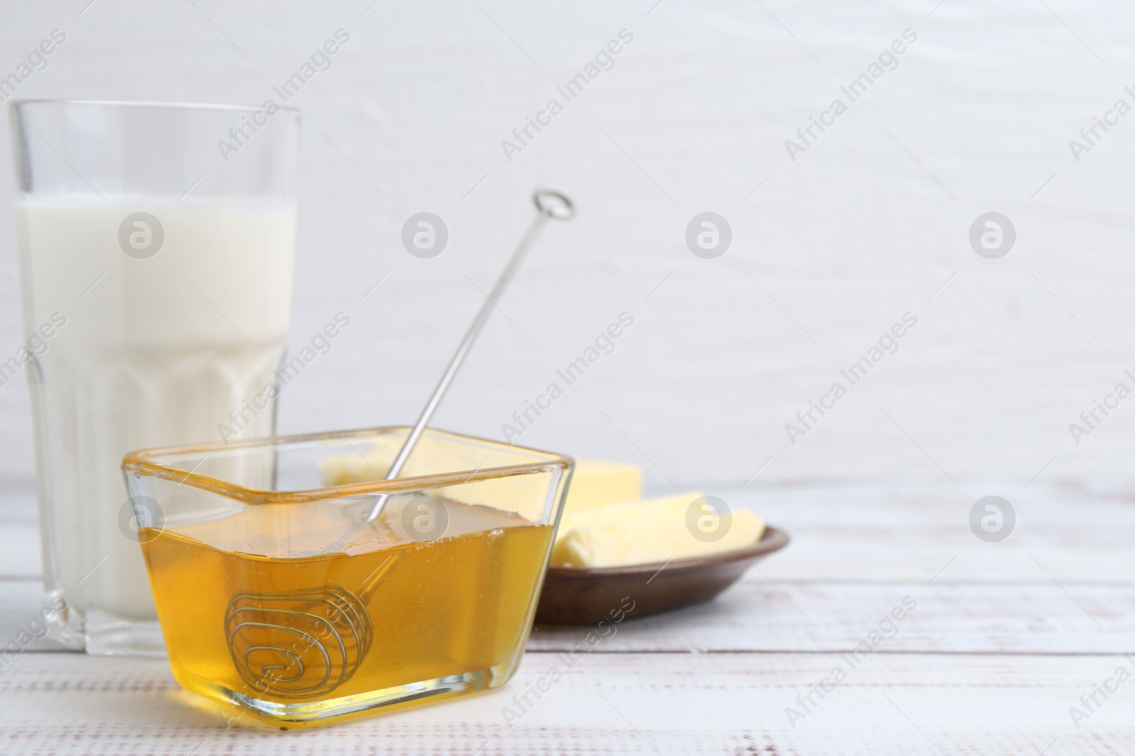 Photo of Sweet honey, butter and milk on white wooden table, closeup. Space for text