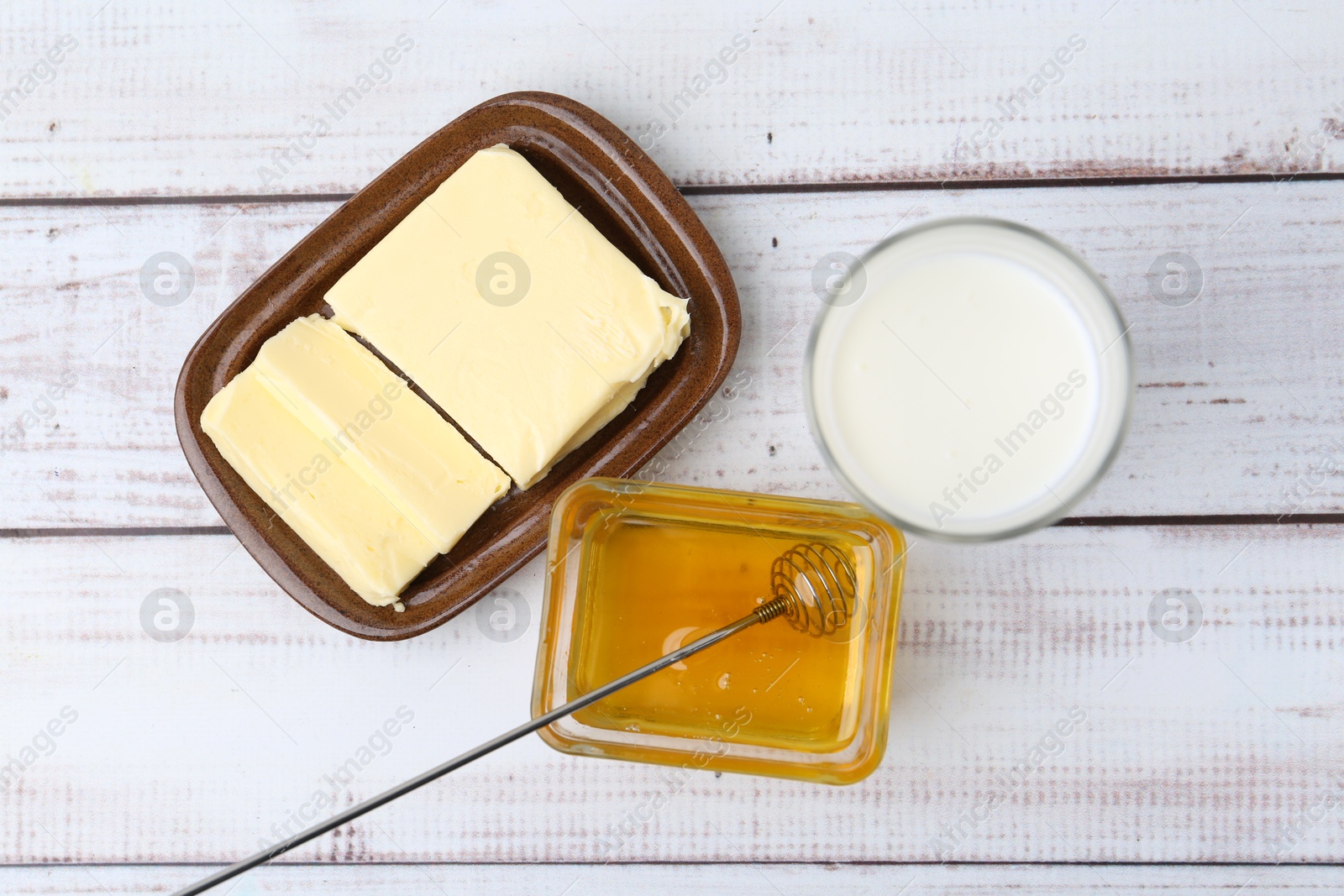 Photo of Sweet honey, butter and milk on white wooden table, flat lay