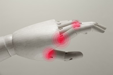 Image of Joint inflammation. Wooden mannequin hand on grey background, closeup. Toned in black-and-white with color areas on fingers