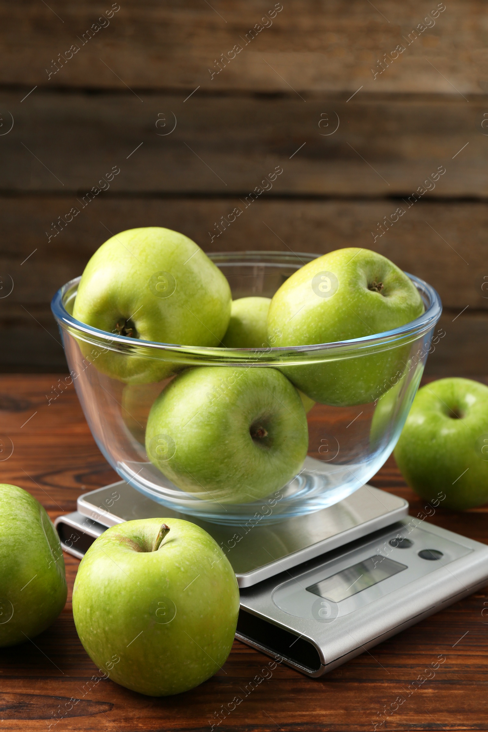 Photo of Electronic kitchen scale with bowl of green apples on wooden table, closeup