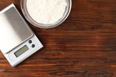 Photo of Electronic kitchen scale and bowl with flour on wooden table, flat lay. Space for text